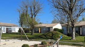 A playground with a seesaw and swings, surrounded by houses with tiled roofs. - 2 - Le Martin-Pêcheur - Village vacances (Maché)
