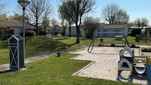 A playground with sand and grass, a wooden play structure, and a small shed. - 2 - Le Martin-Pêcheur - Village vacances (Maché)