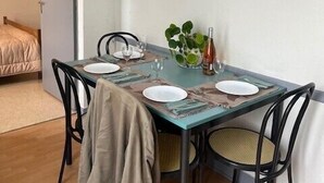 A dining area with a table set for four, chairs, a plant, and a small painting on the wall. - 2 - Le Martin-Pêcheur - Village vacances (Maché)