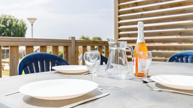 A table set outdoors with a bottle, pitcher, and glasses, surrounded by blue chairs. - 16 - Le Colibri - Village vacances (Maché)