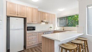 Une cuisine moderne avec des meubles en bois clair, des plans de travail blancs, un four à micro-ondes encastré et une fenêtre donnant sur un paysage verdoyant.