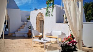 Un'area relax all'aperto riparata, con mobili bianchi, una scala in pietra e un edificio bianco con un arco.
