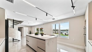 Una cocina moderna con una isla de mármol, armarios elegantes y un amplio ventanal con vistas al exterior.