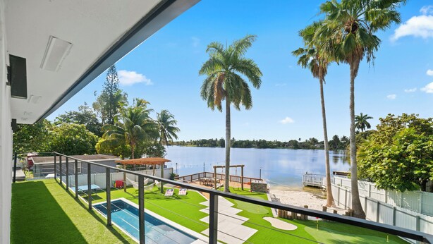 Zona de piscina con césped artificial, una piscina pequeña y vistas a un lago con palmeras.