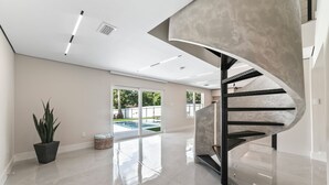 Un interior moderno con una escalera de caracol, una planta grande en maceta y vistas a una piscina.