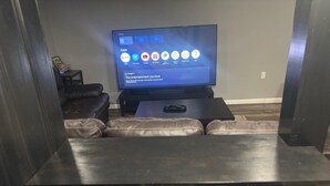 A modern living room with a flat-screen TV displaying a home screen, a leather couch, and a small coffee table.