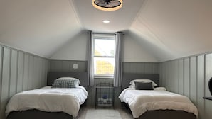 A small, modern attic bedroom with two single beds, a skylight, and a simple, functional design.