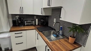 A compact kitchen with white cabinets, a wooden countertop, a sink, and a small potted plant.