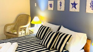 Ein Hotelzimmer mit einem Bett, ausgestattet mit gestreifter, marineblauer und weißer Bettwäsche, einem Korbstuhl, einem Nachttisch mit Lampe und Wandbildern von Meeresbewohnern.