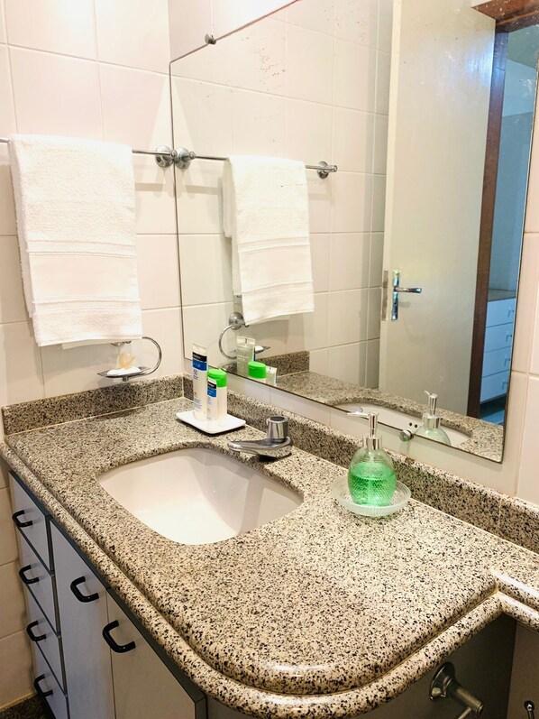 Een badkamer met een granieten aanrecht, een wastafel, een spiegel en twee witte handdoeken aan handdoekhouders.