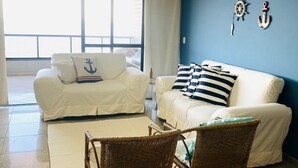 Ein Wohnzimmer mit zwei weißen Sofas, einem Couchtisch und Korbstühlen. An den Wänden befinden sich maritime Dekorationen.