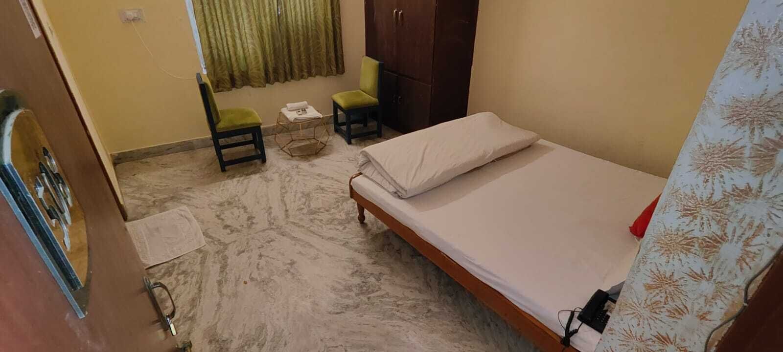 Una stanza modesta con un letto, due sedie, un armadio in legno e una finestra con tende.