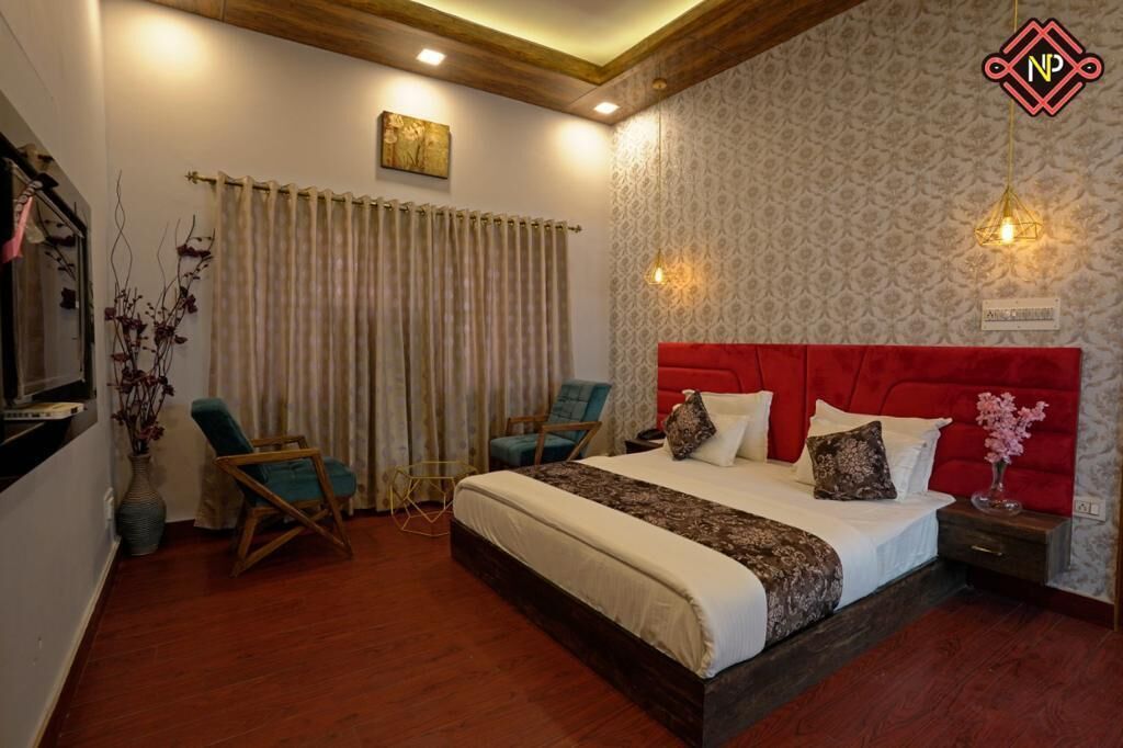 A bedroom with a large bed, two chairs, a nightstand, a vase with flowers, and a wall-mounted artwork.