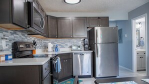 A modern kitchen with dark cabinets, stainless steel appliances, and a tiled backsplash.
