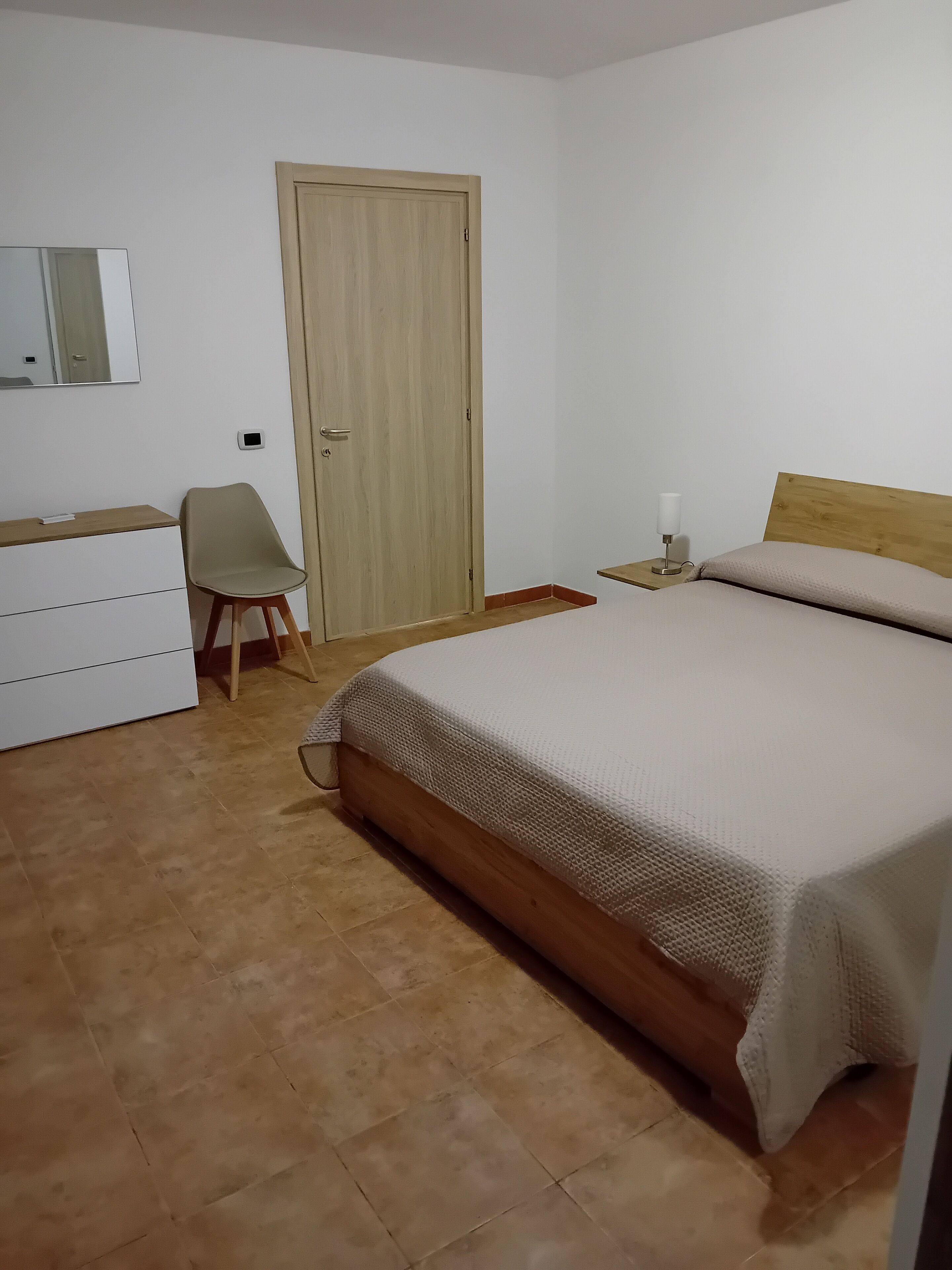 Ein Schlafzimmer mit Bett, Stuhl, Kommode, Nachttisch und einer Tür.