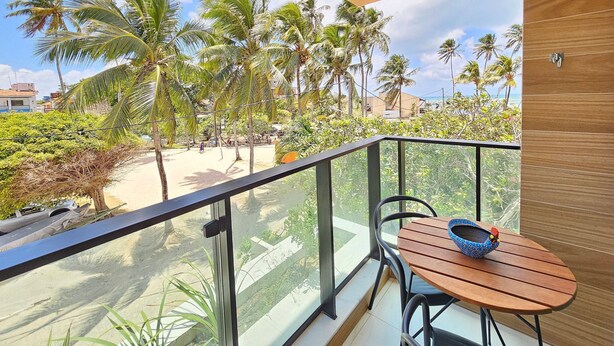 Een balkon met een houten tafel en stoelen, met uitzicht op een strand met palmbomen en een heldere lucht.