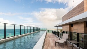 Een zwembadterras met uitzicht op de oceaan, een houten terras en een glazen balustrade.