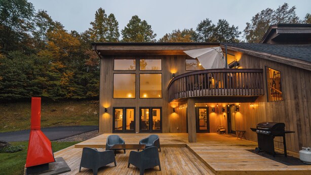 A modern wooden house with a deck, outdoor seating, and a barbecue area.