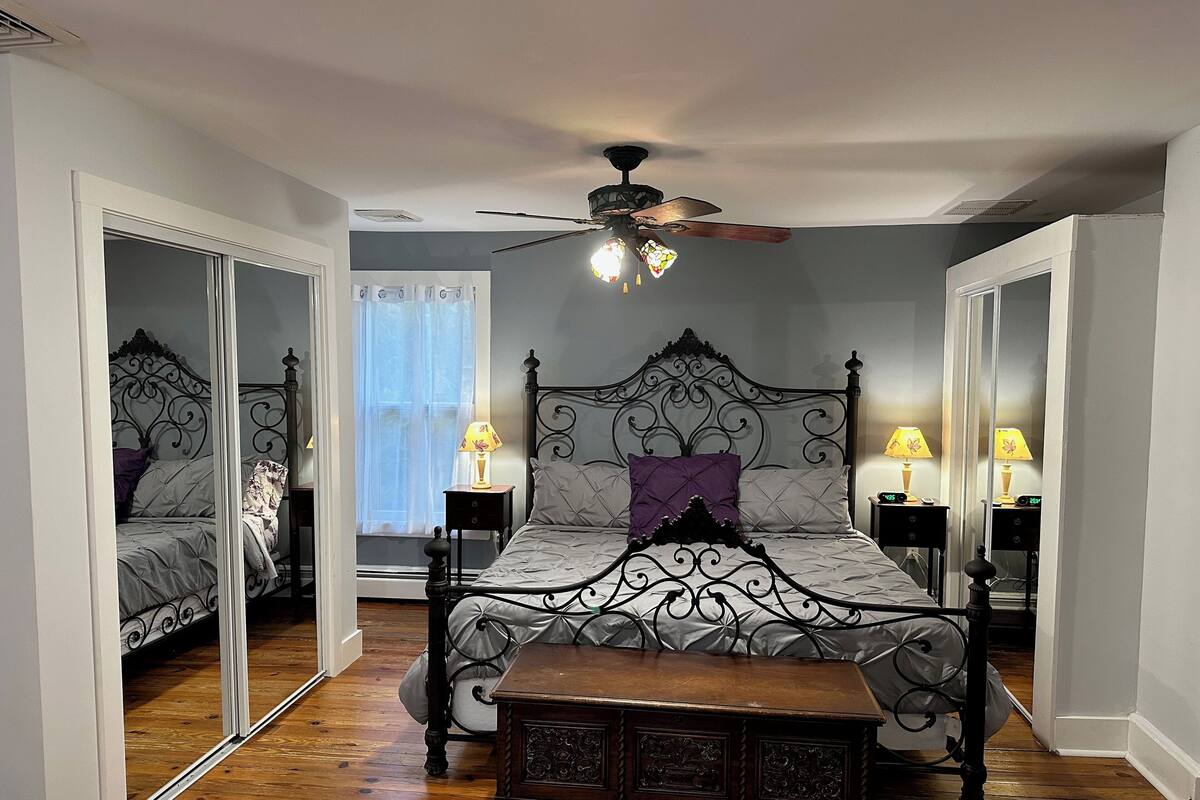 A bedroom with a four-poster bed, a ceiling fan, two bedside tables with lamps, and a wooden bench.
