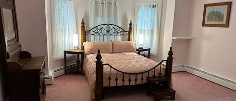 A bedroom with a four-poster bed, two bedside tables, a ceiling fan, and a window with sheer curtains.