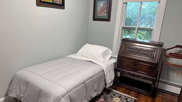 A bedroom with a single bed, a dresser, a window with a view of greenery, and two framed pictures on the wall.