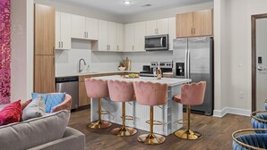 A modern kitchen with white cabinets, stainless steel appliances, and a central island with pink bar stools.