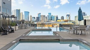 A rooftop pool with lounge chairs and a city skyline view.