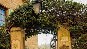 A stone archway with a plaque and a metal gate, leading to a tiled pathway.