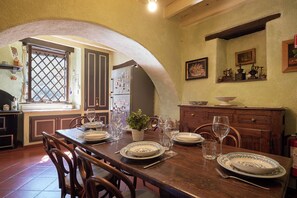 A dining area with a wooden table set for four, surrounded by chairs. A refrigerator and a window with a lattice design are visible in the background.