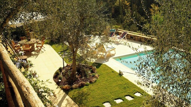 A pool area with lounge chairs and a table, surrounded by trees and a well-maintained lawn.