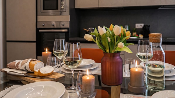 Una mesa de comedor dispuesta con platos, vasos, velas, un florero con flores y una hogaza de pan.