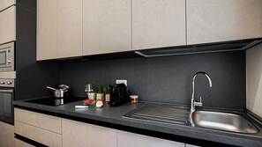 Una cocina moderna con encimera negra, pileta de acero inoxidable y varios electrodomésticos, incluyendo una cafetera y un hervidor.
