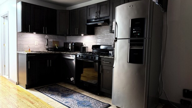 A modern kitchen with dark cabinets, stainless steel appliances, and a black and blue rug.