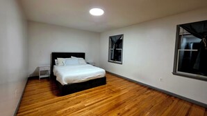 A bedroom with a bed, a nightstand, a window with curtains, and a wooden floor.