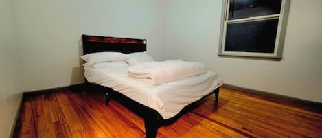 A single bed in a room with wooden flooring and a window.