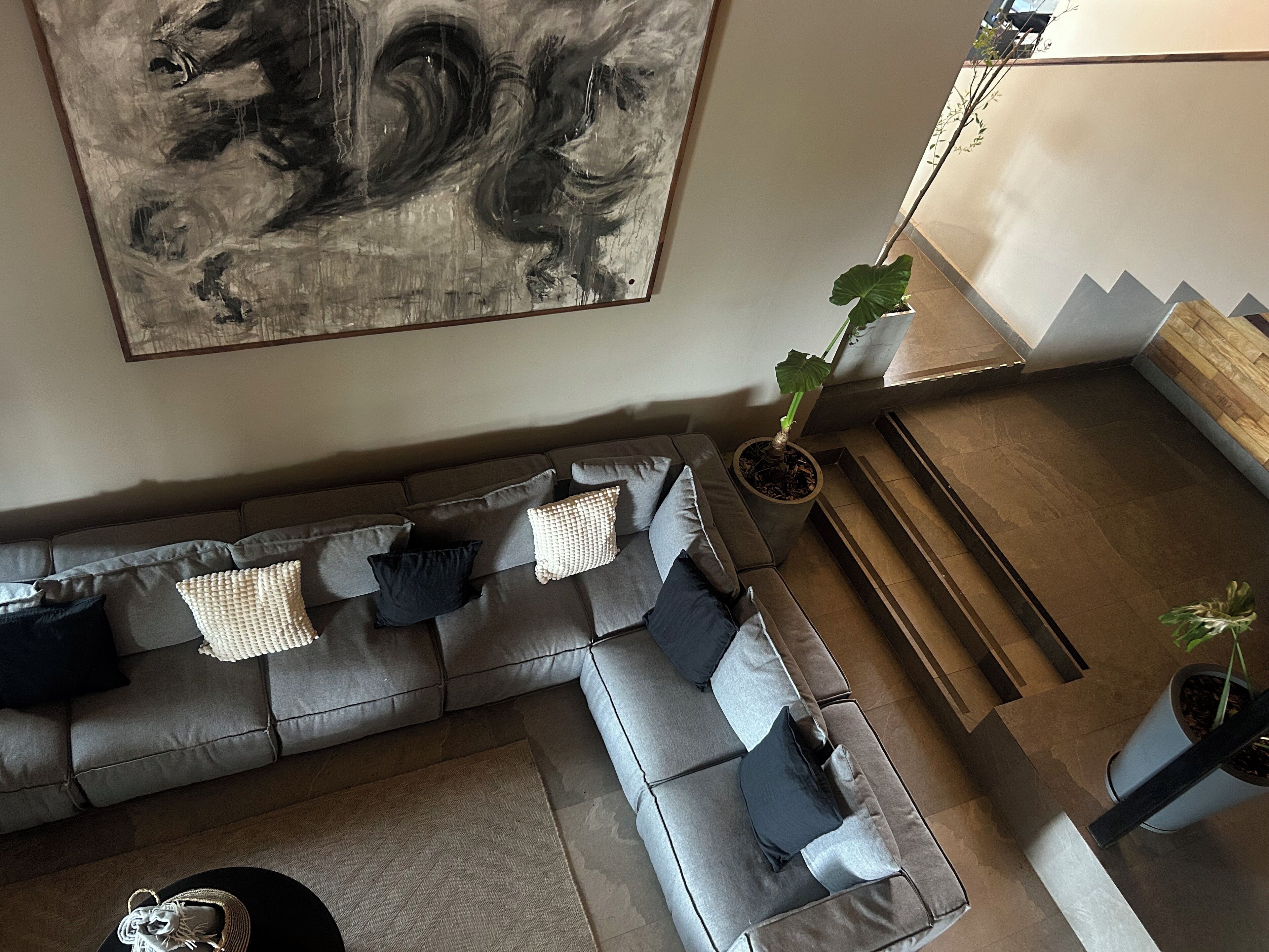 A modern living room with a grey sectional sofa, a large abstract painting, and a staircase leading to an upper level.