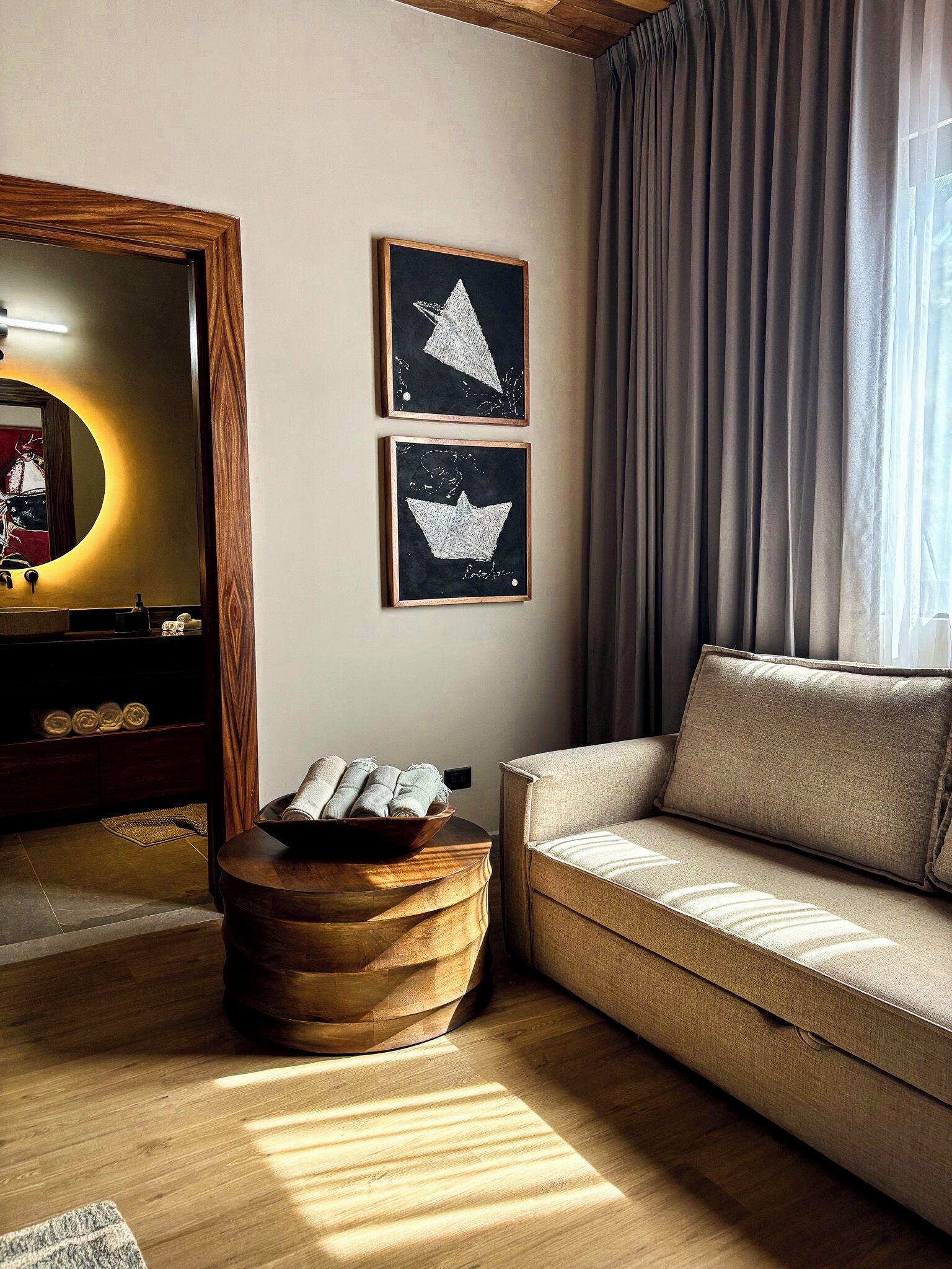 A modern living room with a sofa, a wooden side table with towels, a mirror, and two framed artworks on the wall.