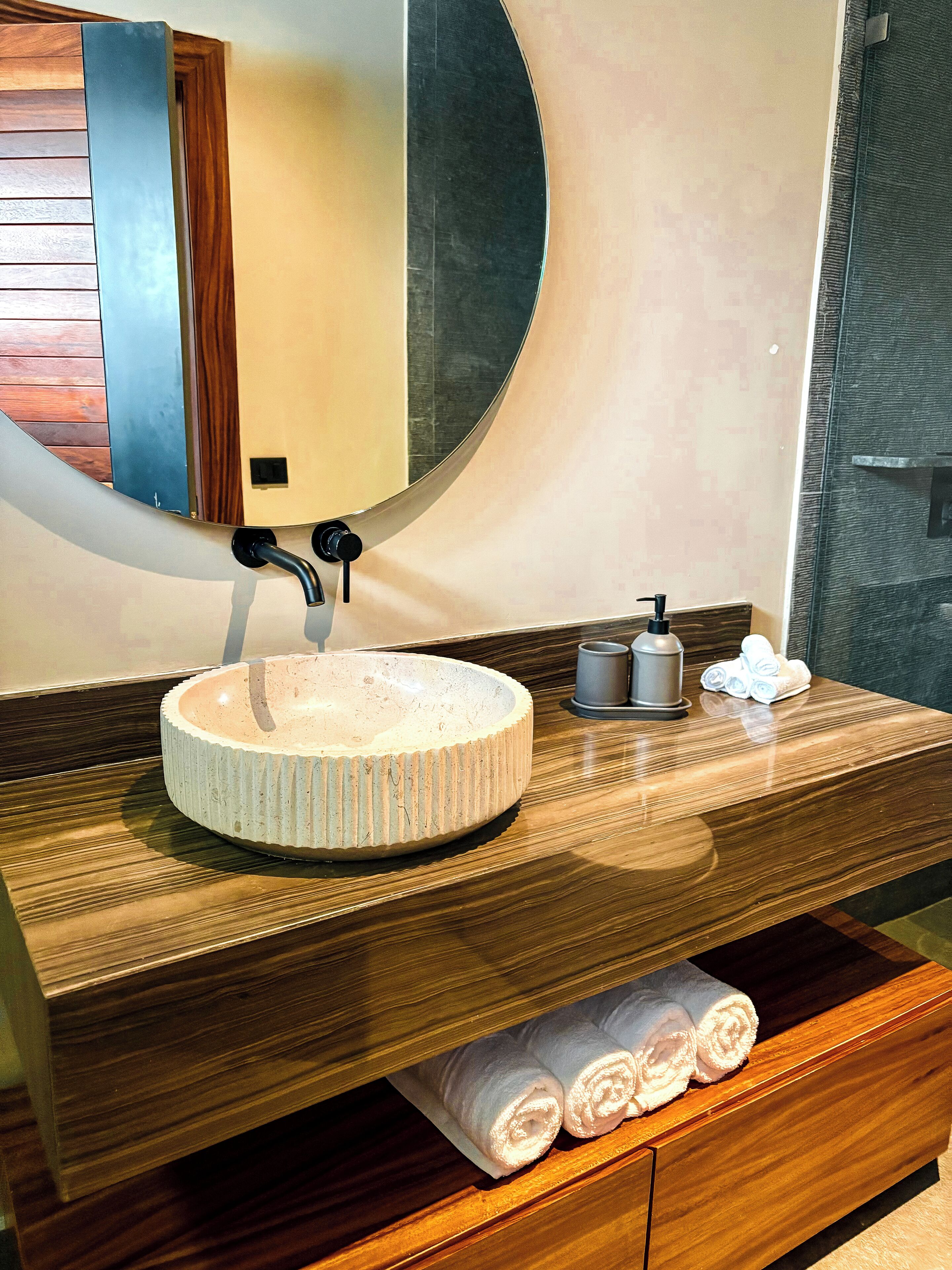 A bathroom with a round sink, a mirror, a towel rack, and a soap dispenser.