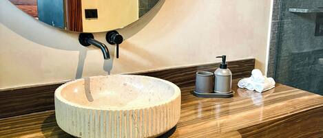 A bathroom with a round sink, a mirror, a towel rack, and a soap dispenser.