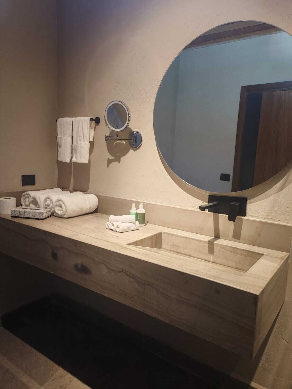 Une salle de bain avec un meuble-lavabo en bois, un miroir rond, un porte-serviettes et un lavabo.
