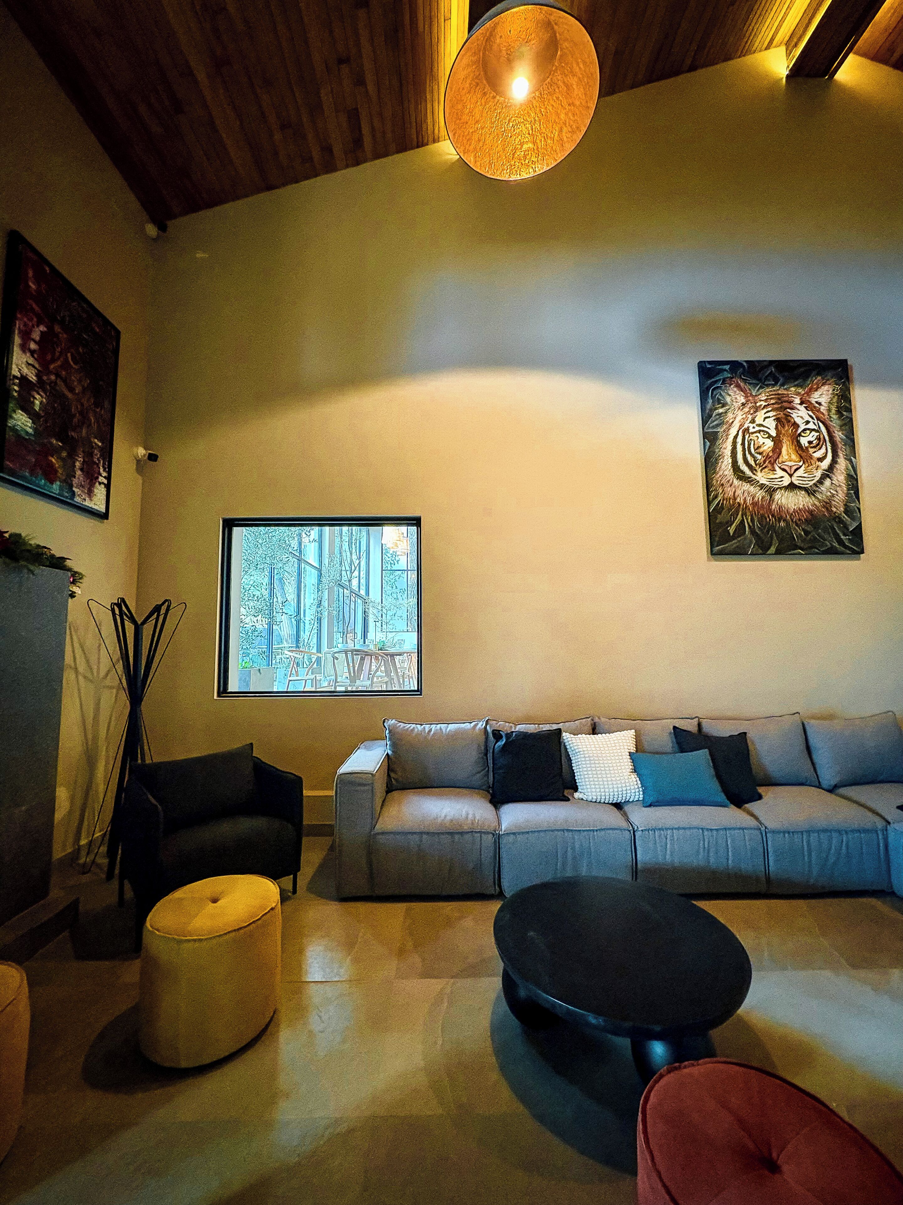 A modern living room with a sofa, ottoman, and coffee table. There is a painting on the wall and a window with a view of trees.