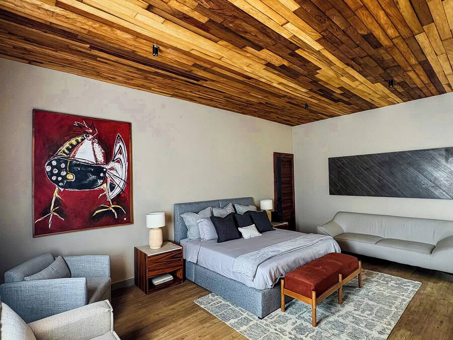 Un dormitorio moderno con techo de madera, una cama grande, un sofá y un cuadro en la pared.