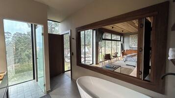 Ein modernes Badezimmer mit einer großzügigen Badewanne, einer Glastür, die auf einen Balkon führt, und Blick ins Freie.