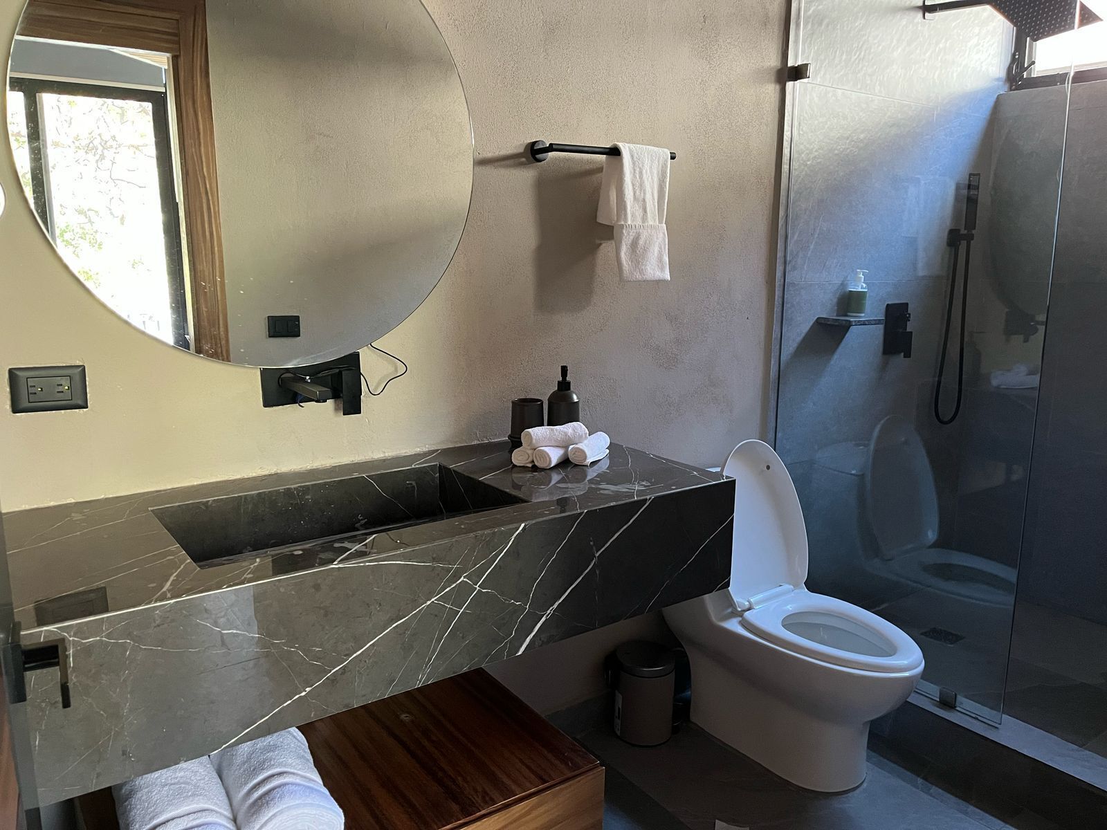 A modern bathroom with a marble sink, a toilet, and a glass shower enclosure.