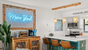 A modern kitchen with a neon sign, wooden accents, and a teal backsplash.