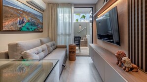 Una sala de estar moderna con un sofá, una mesa de centro de vidrio, un televisor montado y un taburete decorativo de madera.