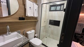 Un baño moderno con ducha acristalada, lavamanos con encimera de mármol, inodoro y toallero con toallas de la marca.