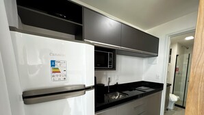 Eine moderne Küche mit einem weißen Kühlschrank, einer schwarzen Mikrowelle und einem Edelstahl-Spülbecken.