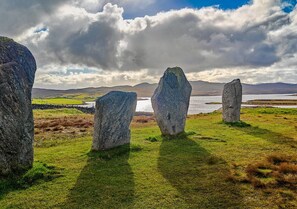 Explore a serene landscape featuring ancient standing stones set amidst rolling hills and a tranquil water body.