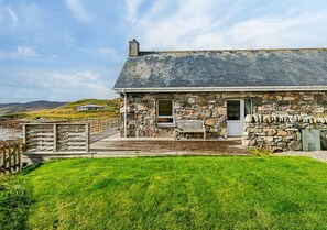 Situated on a grassy area, this charming cottage offers a view of the sea and features a cozy porch with a bench.